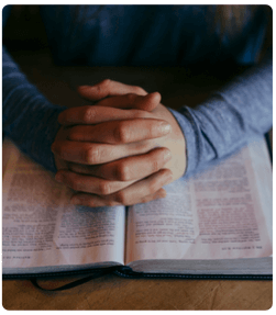 Folded hands praying over open Bible